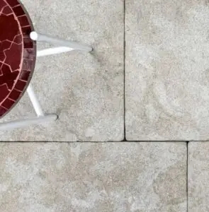 Top edge of a round table with a red mosaic top and white legs on a concrete patio surface.