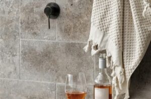 Wine bottle and a glass of rosé on a gray tiled surface, with a textured beige towel draped nearby.