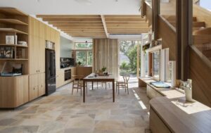Open-concept kitchen with wooden cabinets, a central dining table, and a glass wall opening to a garden.