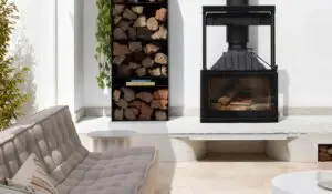 Outdoor patio with a black glass-front wood-burning fireplace, stacked firewood shelves, and a light tufted sofa nearby.