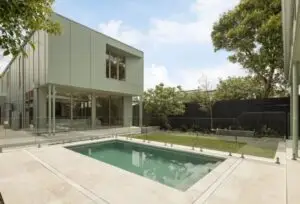 Modern two-story house with large glass windows and a rectangular pool in the backyard, enclosed by a glass fence.