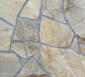Stone wall with irregular, multicolored flagstones joined by gray mortar lines. Used as a decorative paving or wall surface in natural tones.