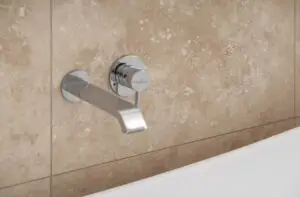 Chrome wall-mounted bathtub faucet with a single lever handle against beige tiled wall, close-up detail.